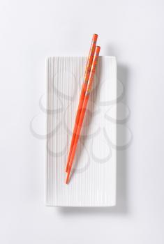 A pair of orange chopsticks on empty white sushi plate