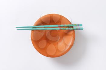 A pair of blue chopsticks on empty terracotta bowl