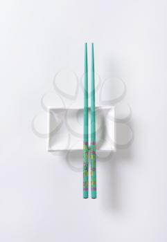 A pair of blue chopsticks on empty soy sauce dish