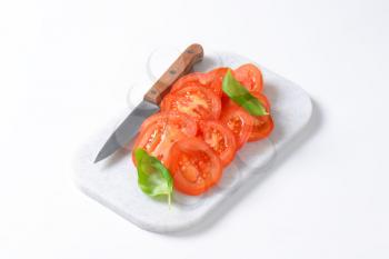 tomato slices and kitchen knife on plastic cutting board