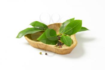 Sprig of bay leaves and peppercorns in triangle wooden bowl