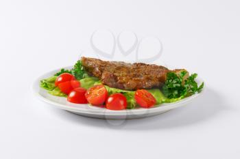marinated pork steak with vegetable garnish on white plate