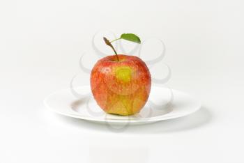washed red apple with leaf on white plate