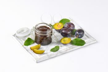 jar of plum jam and fresh plums on wooden cutting board