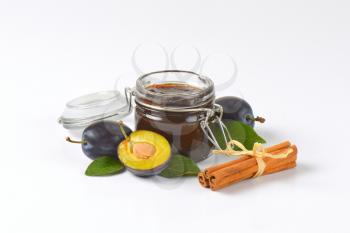 jar of fresh plum jam, ripe plums and cinnamon on white background