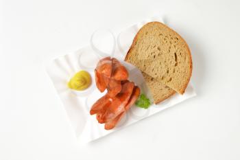 roasted sausages, mustard and bread slices on paper plate