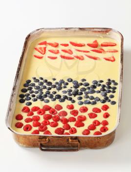 raw batter with fresh raspberries, blueberries and strawberries in a baking tin