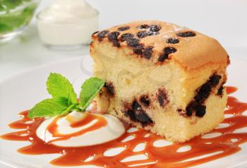 Piece of sponge cake with chocolate chips, cream and caramel sauce on a white plate