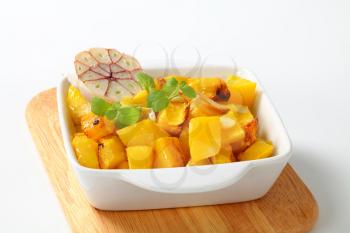 Roasted pumpkin cubes and garlic in square baking dish