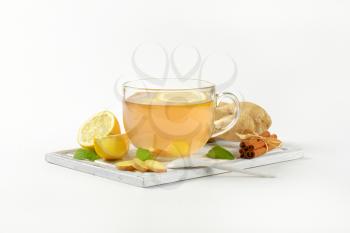 cup of ginger tea with lemon, fresh ginger root and cinnamon sticks on wooden cutting board