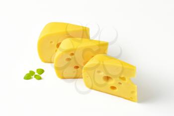 three wedges of yellow medium-hard cheese with eyes on white background