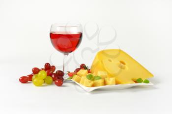 yellow medium-hard cheese with eyes, glass of red wine and fresh grapes