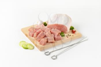 Diced lean raw pork on cutting board and metal skewers next to it