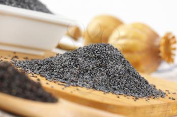 heap of whole poppy seeds on wooden cutting board