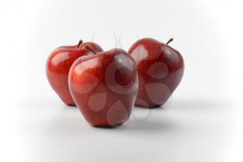 three glossy red apples on off-white background