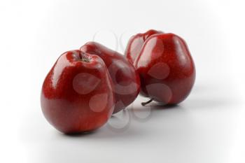 four glossy red apples on off-white background