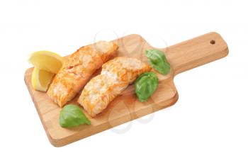 two cooked salmon fillets on wooden cutting board