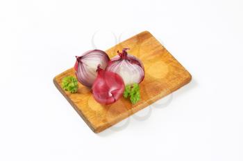 whole and halved red onions on wooden cutting board