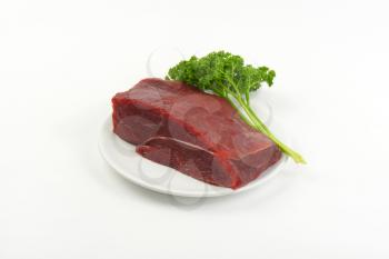 raw beef meat and fresh parsley on white plate