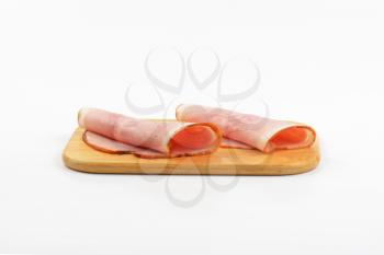 two ham slices rolled up on wooden cutting board