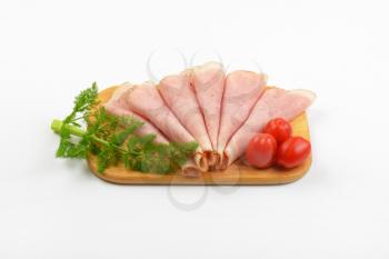 ham slices with dill an cherry tomatoes on wooden cutting board
