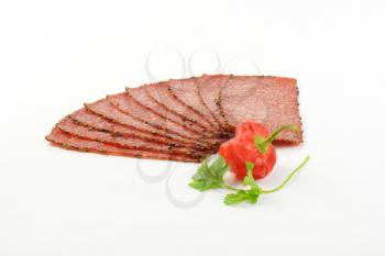 Thin slices of pepper coated salami on white background