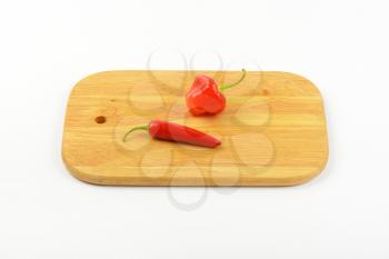 two red hot chili peppers on wooden cutting board