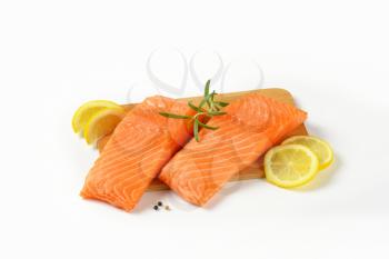 two raw salmon fillets, lemon and rosemary on cutting board