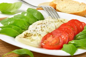 sliced mozzarella, tomatoes and fresh basil on plate
