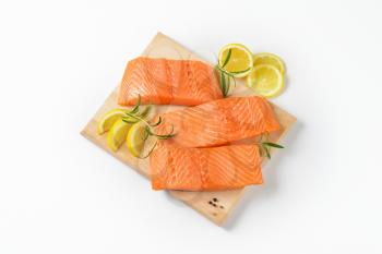 three raw salmon fillets, lemon and rosemary on cutting board