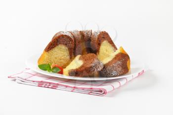 sliced marble bundt cake on white plate and checkered dish towel