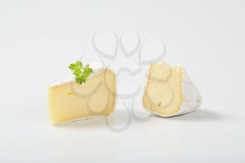 two slices of white rind cheese with parsley on white background