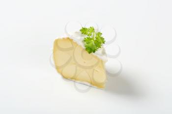 slice of white rind cheese with parsley on white background