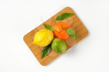 lemon, lime and tangerine on wooden cutting board