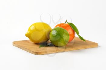 lemon, lime and tangerine on wooden cutting board