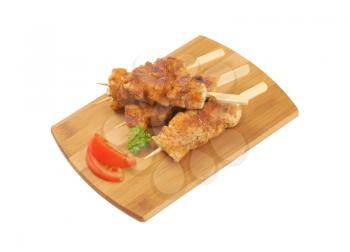 four spicy chicken skewers on wooden cutting board