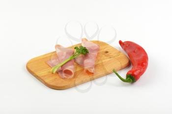 slices of pork ham with parsley and red pepper on wooden cutting board