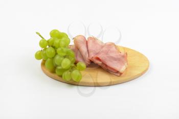 ham slices with bunch of white grapes on oval wooden cutting board