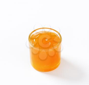 glass of apricot jam on white background