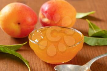 fresh apricots and bowl of apricot jam on wooden table - close up