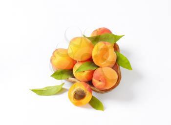 bowl of ripe apricots with leaves on white background