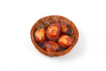 basket of Easter eggs decorated with fresh leaves and boiled in onion peels on white background