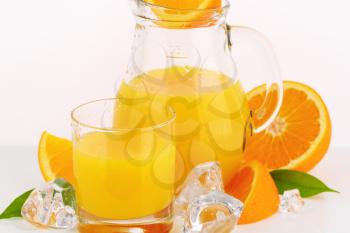 glass and jug of fresh orange juice on white background - close up