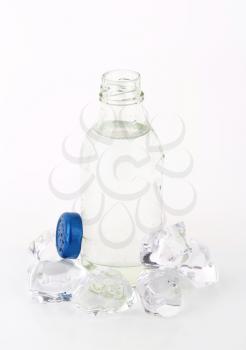bottle of fresh water and ice cubes on white background
