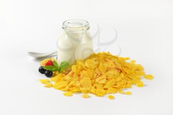 pile of corn flakes and glass of white yogurt on white background
