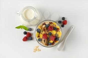 bowl of mixed breakfast cereals with fresh raspberries and blueberries, and jug of milk