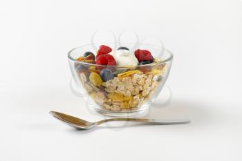 bowl of mixed breakfast cereals with fresh raspberries and blueberries and yogurt