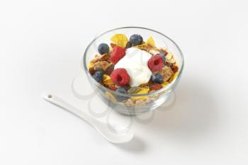 bowl of mixed breakfast cereals with fresh raspberries and blueberries and yogurt