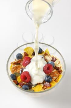 milk pouring into bowl of breakfast cereals with berry fruit