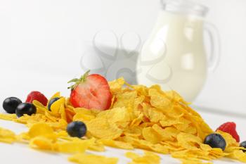 jug of milk and corn flakes with berry fruits on white background - close up